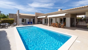 A swimming pool with a tiled deck, outdoor furniture, and a covered patio area.