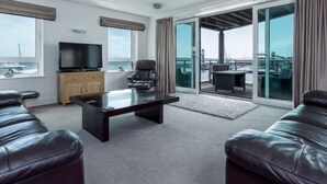 A modern living room with a flat-screen TV, leather sofas, a glass door leading to a balcony, and a view of the sea. - Panorama - 180-Degree Harbour Views (Poole)