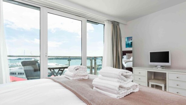 A hotel room with a large bed, a TV, a desk, and a view of the sea. - Panorama - 180-Degree Harbour Views (Poole)