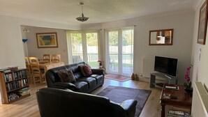 A living room with a black leather sofa, a wooden coffee table, a bookshelf, and a television.