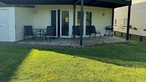 A covered patio area with a table and chairs, a sliding glass door, and a grill.