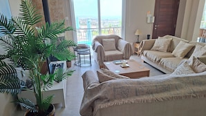 Un salón con una planta grande, dos sofás, una mesita de centro y vistas al exterior a través de un ventanal corredero.