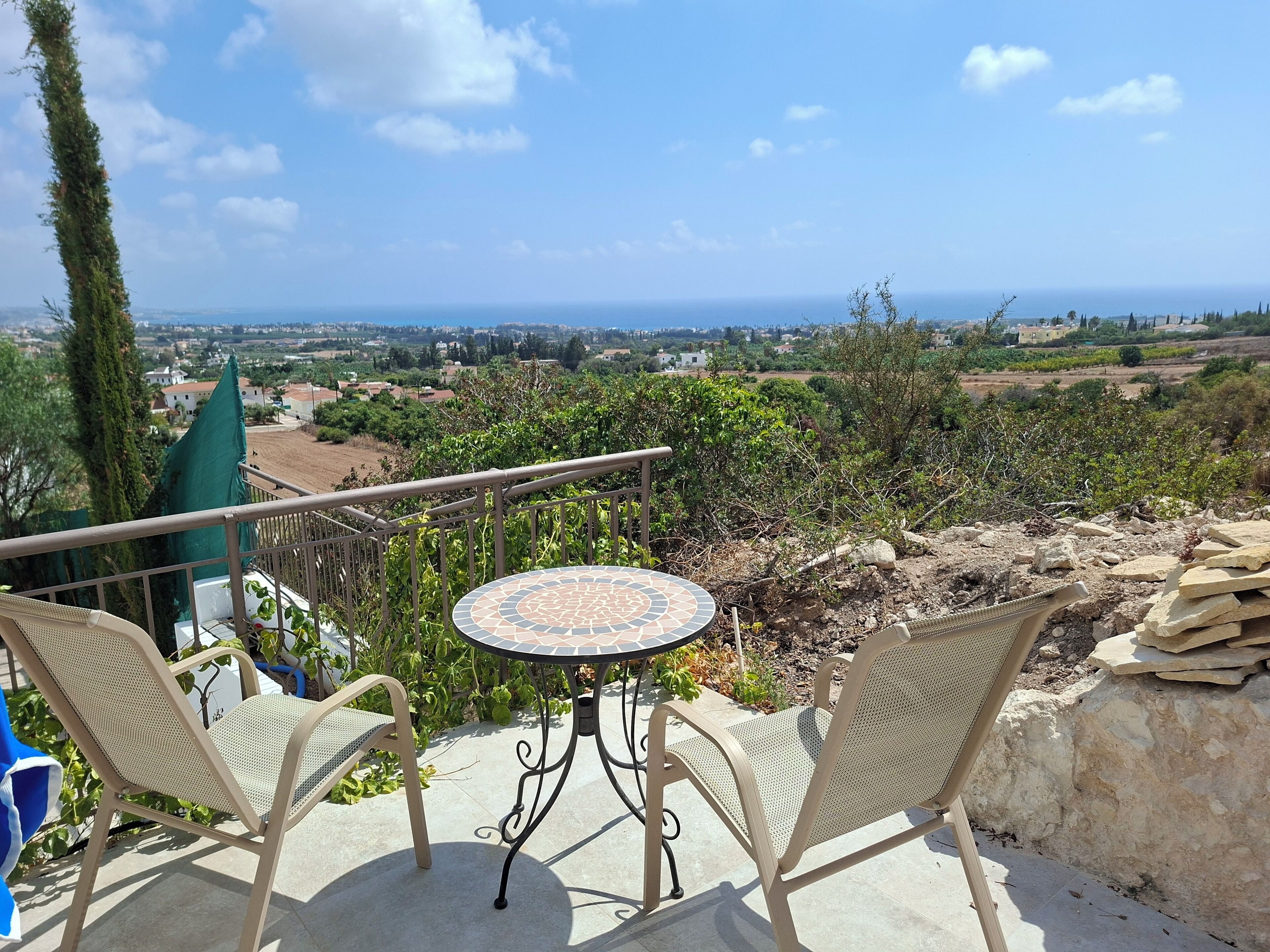 Une terrasse avec une table ronde et deux chaises, offrant une vue panoramique sur un paysage pittoresque composé de champs et de bâtiments éloignés.