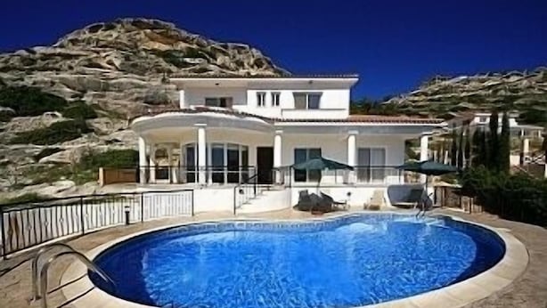 Una casa moderna con piscina, rodeada por un patio de piedra y un paisaje montañoso.