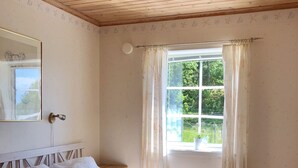 Quarto com teto de madeira, cama com roupa de cama branca, janela com cortinas e espelho na parede.