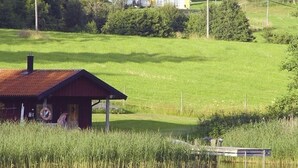 Uma cabana rústica à beira de um lago, com um cais e uma casa ao fundo.