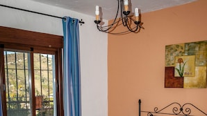 Une chambre à coucher avec un lit, une literie bleue, des serviettes orange, une table de chevet, un tableau et une fenêtre avec des rideaux.