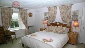 A bedroom with a large bed, two bedside tables with lamps, a chair, a dresser, and floral curtains. - Yorkshire Dales Stone Cottage. Wonderful Location for Walking in Swaledale (Grinton)