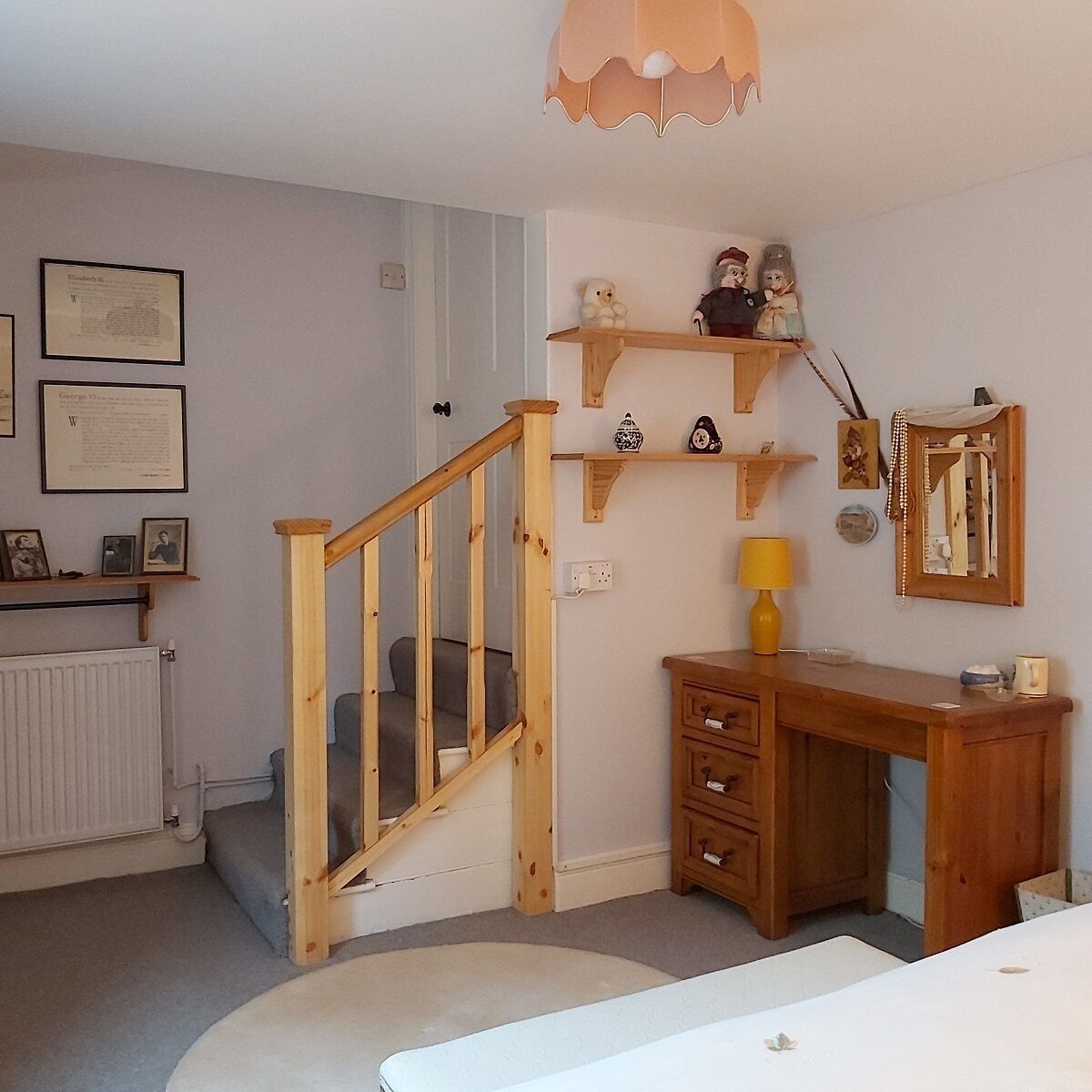 Une pièce avec un escalier en bois, un bureau doté de tiroirs, une petite étagère ornée d’objets décoratifs et des certificats encadrés accrochés au mur.