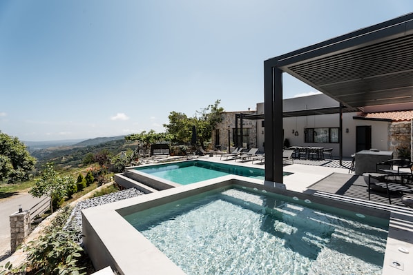 Un espace piscine extérieur moderne offrant une vue sur la campagne, avec des murs en pierre et du mobilier d’extérieur.