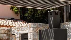 An outdoor kitchen with a stone wall, a built-in grill, and bar stools. - Eumelia Iconic Villa, with Heated Pool & Whirlpool, BBQ, Close to amenities (Rethymno)
