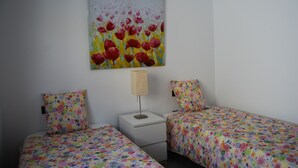 Une chambre à coucher avec deux lits, chacun recouvert d’une courtepointe aux motifs floraux colorés, une table de chevet avec une lampe et un tableau représentant des fleurs rouges accroché au mur.