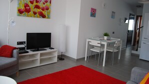 Un salon moderne avec un téléviseur à écran plat, un tapis rouge, une table à manger avec des chaises et un canapé blanc.