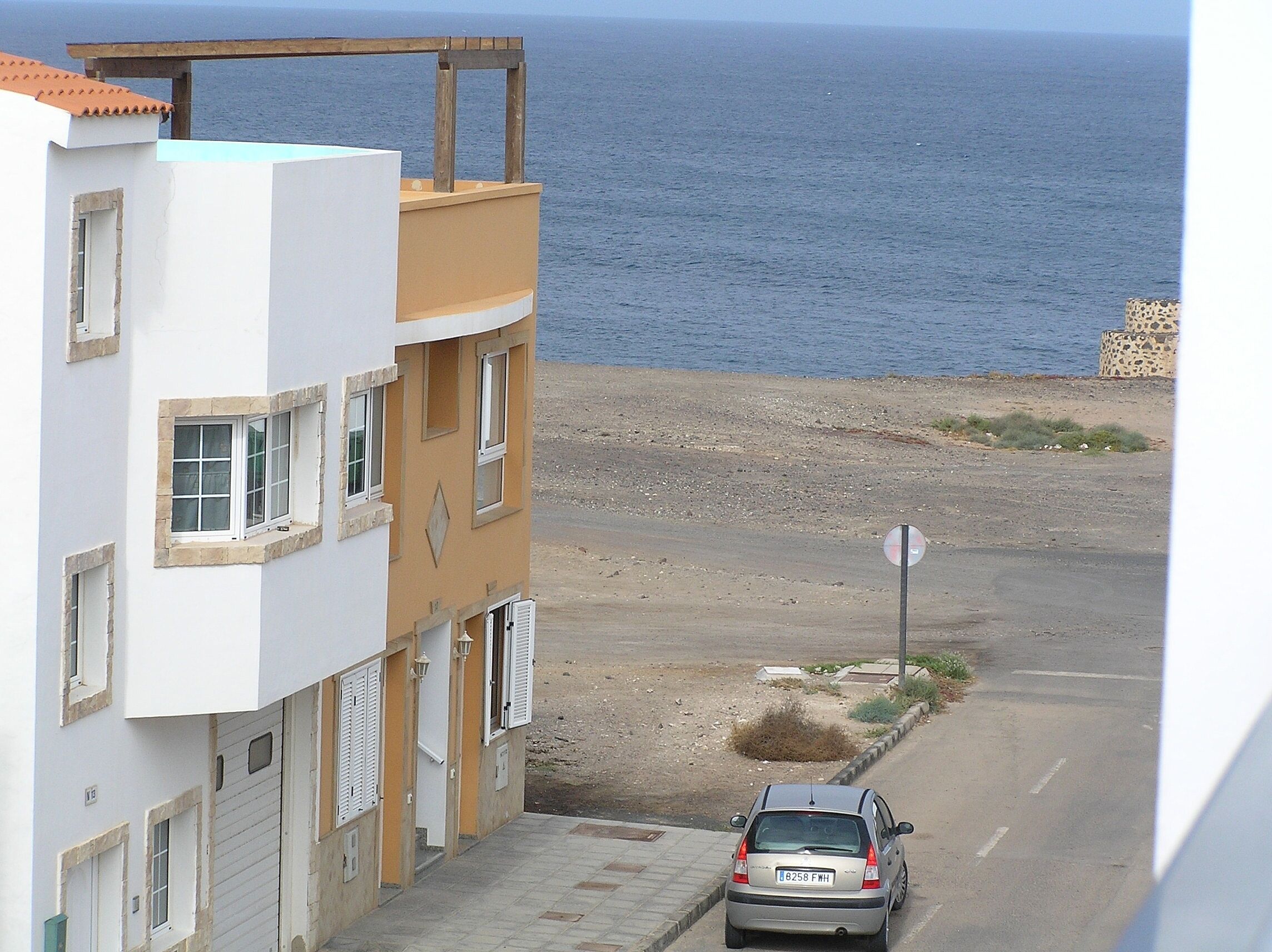 A coastal road with a parked car, buildings with balconies, and a view of the sea.