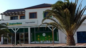 Un supermarché SuperDino avec un toit recouvert de tuiles, un vélo garé à l'extérieur et un palmier au premier plan.