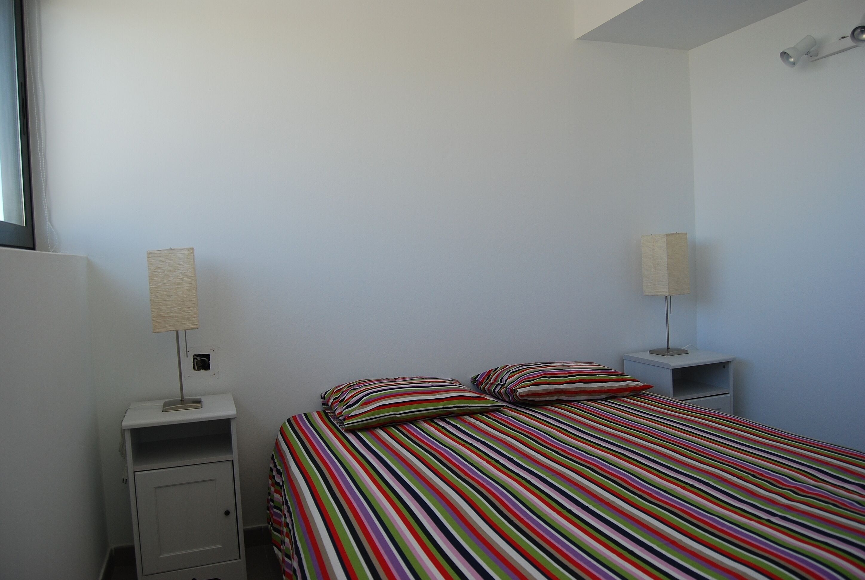 Une chambre à coucher avec une couvre-lit à rayures, deux tables de chevet avec des lampes et une petite armoire.