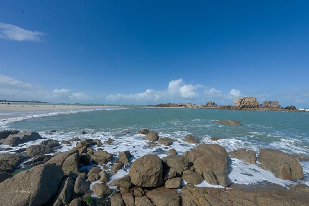 A rocky beach with waves crashing onto the shore, a clear sky, and distant rocky formations.