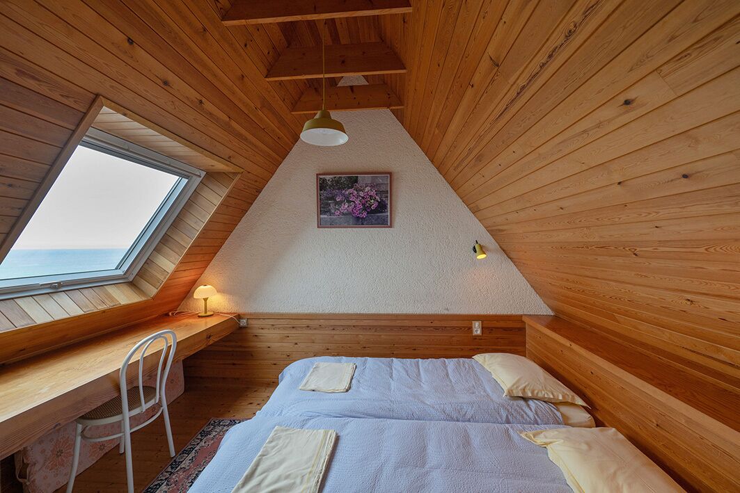 Une pièce chaleureuse aux murs lambrissés, comprenant un lit, un bureau et une chaise.