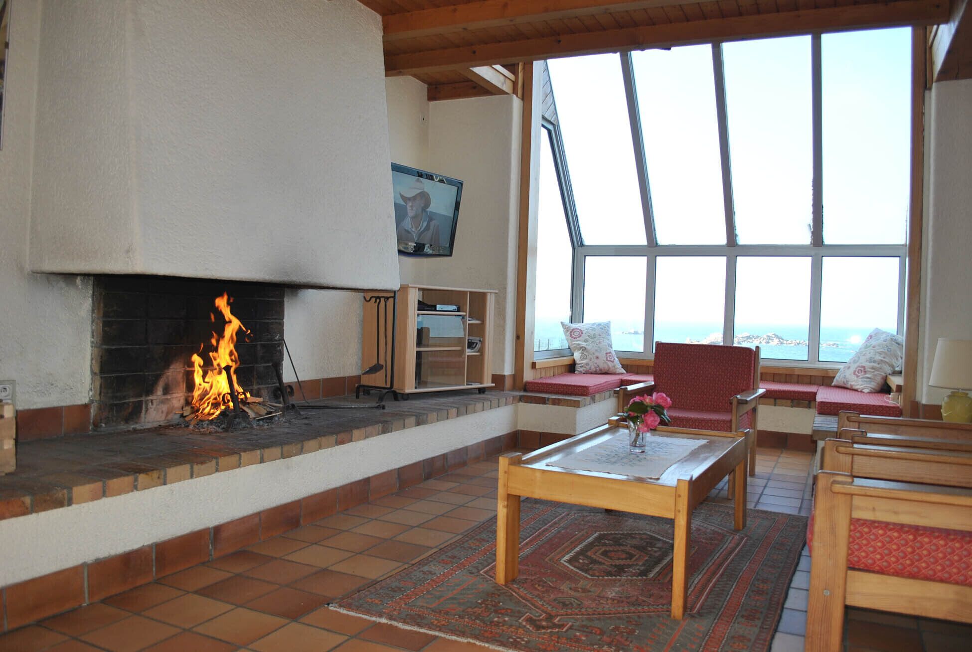 Ein gemütliches Wohnzimmer mit Kamin, Holzmöbeln und großen Fenstern mit Aussicht.