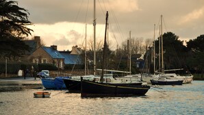 Un port où plusieurs bateaux sont amarrés, un bâtiment avec un toit bleu et un ciel nuageux.