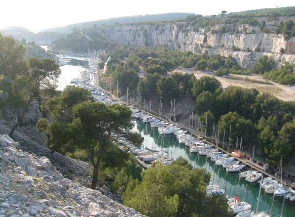 Un port de plaisance où des bateaux sont amarrés le long d’une rive, entouré de falaises et d’arbres.