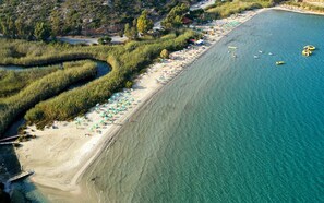 An aerial view of a beach with clear turquoise water, a sandy shore, and a line of umbrellas and beach chairs.