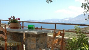 Una mesa de piedra con sillas, una planta en maceta y una botella verde en un balcón con vistas a un paisaje montañoso.