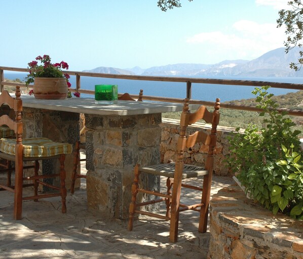 A stone table with chairs, a potted plant, and a green bottle on a balcony overlooking a mountainous landscape.