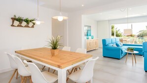 Un espace de vie moderne comprenant une table à manger en bois, des chaises blanches, un canapé bleu et un coin cuisine avec des placards et un luminaire suspendu.