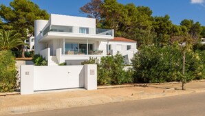 Une maison moderne à deux étages, dotée d’un toit plat, de grandes fenêtres et d’un balcon.