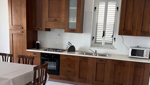 A kitchen with wooden cabinets, a gas stove, a microwave, and a dining area with a table and chairs. - GORGEOUS PENTHOUSE WITH SEA VIEW GIUSI BREATHTAKING ... FREE WIFI INTERNET !!! (Balestrate)
