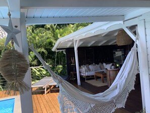 A covered outdoor area with a hammock, lounge chairs, and a pool.