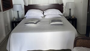 A bed with a canopy, two bedside tables with lamps, and a wicker chair. - SEA VIEW VILLA + OVERFLOW POOL (Deshaies)