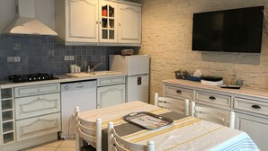 Una cocina con gabinetes blancos, una estufa, un lavabo y un televisor montado en la pared.