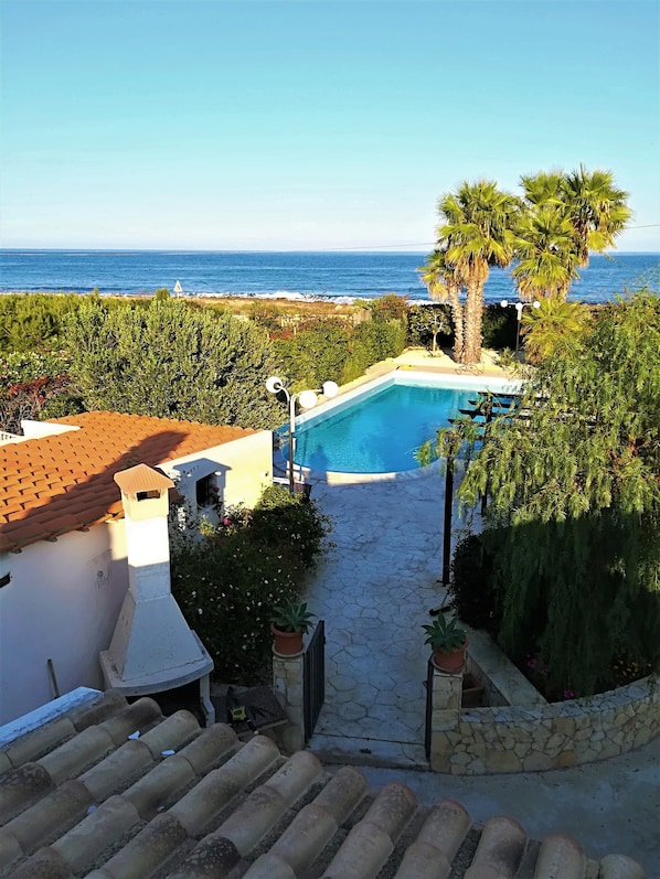 A swimming pool with a view of the ocean, surrounded by greenery and a stone pathway.