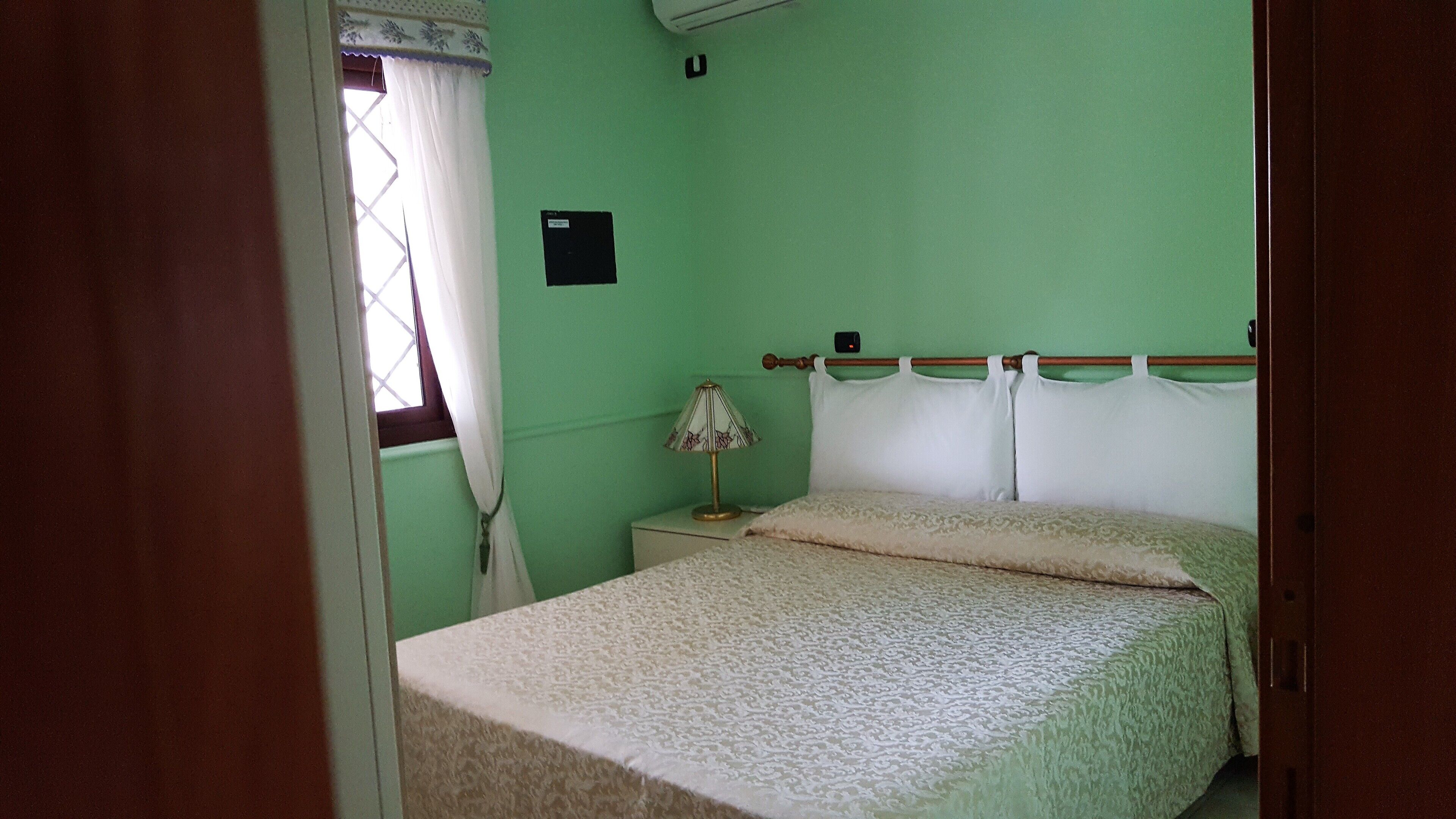 Une petite chambre à coucher simple, avec un lit, une table de chevet, une lampe et une fenêtre avec des rideaux.