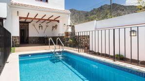 A poolside area with a clear blue pool, a pergola with wooden beams, and a mountain backdrop. - house with pool, barbecue (Nigüelas)