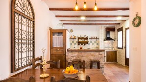 A dining area with a wooden table, chairs, and a bowl of fruit. There is a kitchen in the background with a tiled backsplash and wooden cabinets. - house with pool, barbecue (Nigüelas)