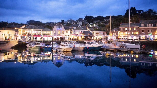 A marina with boats docked, a waterfront promenade, and buildings with illuminated signs.