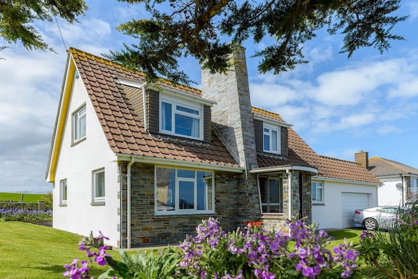 A two-story house with a stone chimney, a brown tiled roof, and a white exterior.