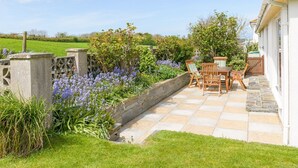 A patio with a stone floor, surrounded by a garden with various plants and flowers.