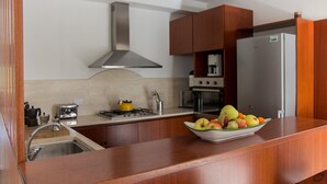 Una cuina moderna amb armaris de fusta, una campana extractora d'acer inoxidable, una cuina de gas, un vàter i un bol de fruita sobre el taulell.