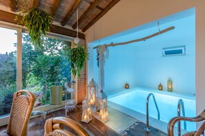 Ein moderner Wellnessraum mit einer großen Badewanne, Korbstühlen, hängenden Pflanzen und dekorativen Laternen.