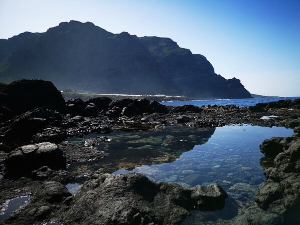 Una costa rocosa con agua cristalina y una montaña al fondo.