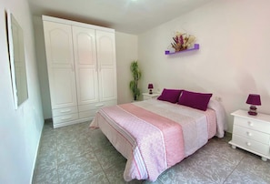 Une chambre à coucher comprenant un lit, des tables de chevet, une armoire et une étagère murale agrémentée d’objets décoratifs.