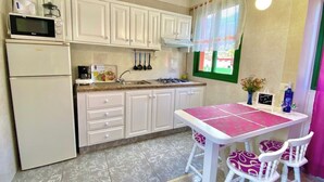 A kitchen with white cabinets, a refrigerator, a microwave, a gas stove, and a table with chairs.