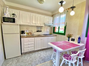 Una cocina con armarios blancos, un refrigerador, un microondas, una estufa a gas y una mesa con sillas.