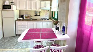 A kitchen with white cabinets, a white refrigerator, a stove, and a sink. There is a table with a pink tablecloth and four chairs.