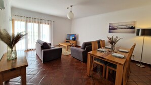 Un salon avec un canapé, une table à manger dressée pour deux personnes, un téléviseur et un tableau accroché au mur.