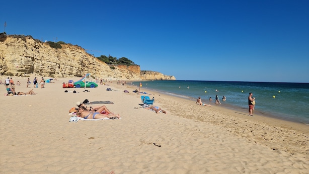 Une plage où des gens se prélassent au soleil et se baignent, une voiture verte et un drapeau.